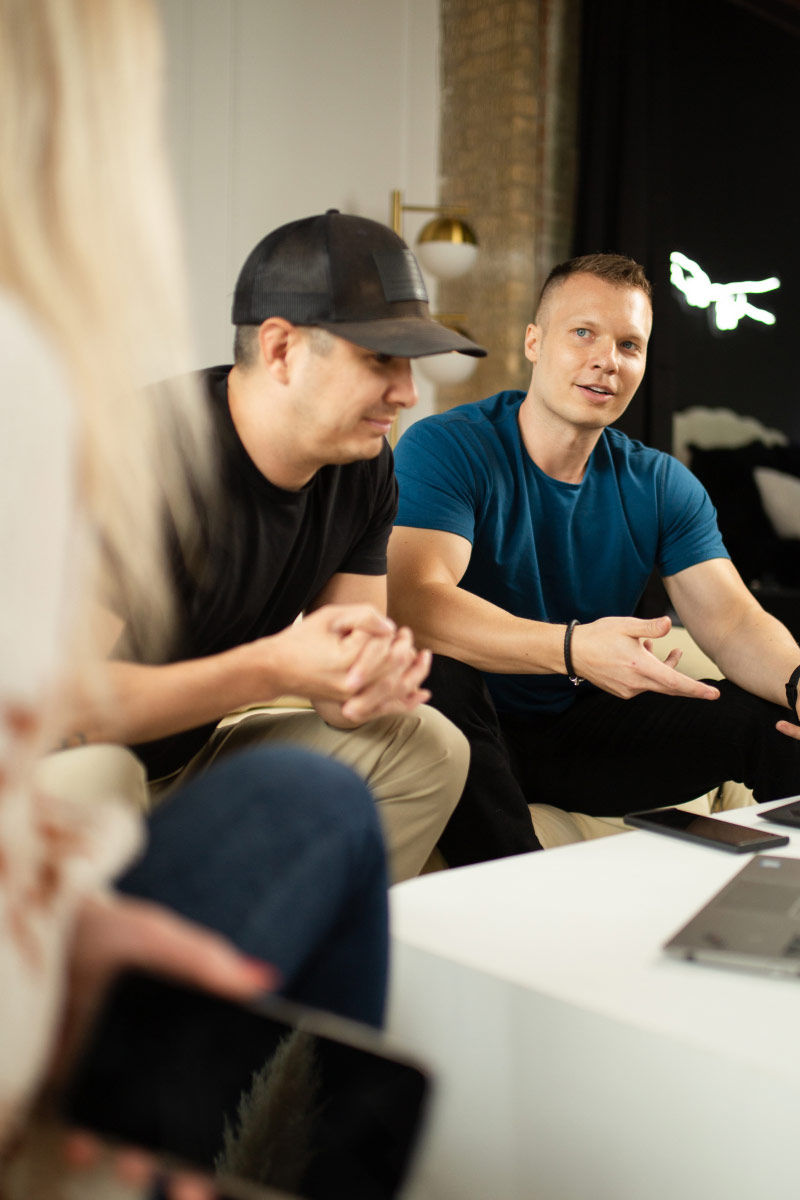 Portrait photo of Tim Welsh chatting with a blonde woman while sitting with other team members.